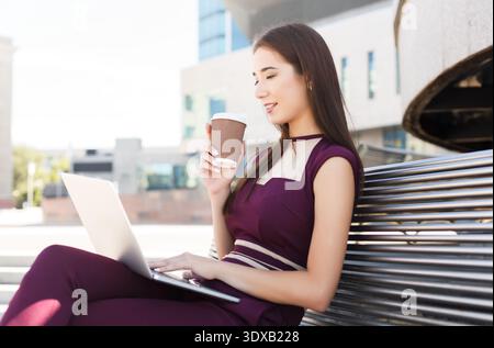 Woman Works on Computer While Enjoying Coffee Outside in a Modern City Setting Stock Photo