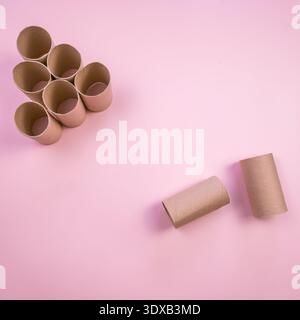 A collection of empty cardboard toilet paper rolls arranged on a pink background. Two rolls are placed separately from the group. Stock Photo