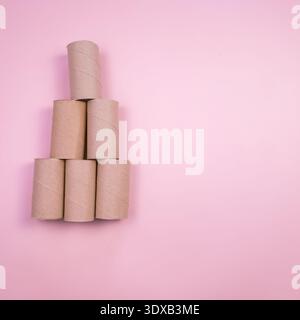 A pyramid of empty toilet paper cardboard tubes arranged on a pink background. The tubes are of varying heights and are stacked in a triangular format Stock Photo
