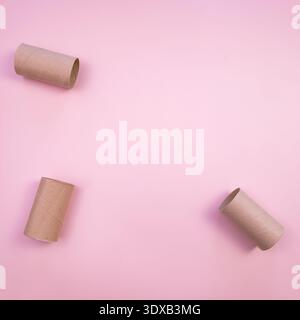 Three empty toilet paper tubes on a pink background. The tubes are cylindrical and made of brown recycled paper. A simple and minimalist composition. Stock Photo
