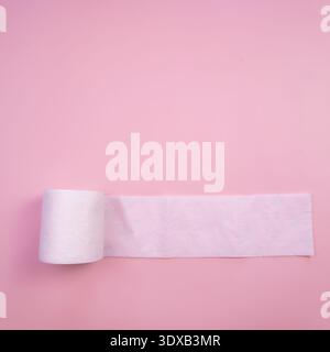 A roll of white toilet paper on a pink background. The paper is partially unrolled, showcasing its soft texture and clean appearance. Stock Photo