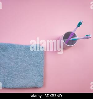 A blue towel and a cup with two toothbrushes on a pink background. The scene is simple and clean, emphasizing hygiene and personal care. Stock Photo