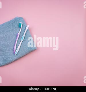Two toothbrushes, one pink and one blue, placed on a gray towel against a pink background. Ideal for dental hygiene concepts. Stock Photo