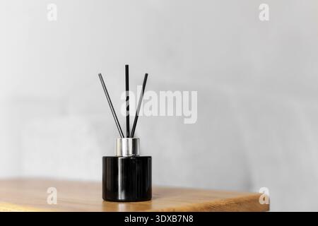 Black reed diffuser on wooden table against light wall. Minimalist home decor with aroma sticks and glass bottle. Modern interior fragrance concept wi Stock Photo