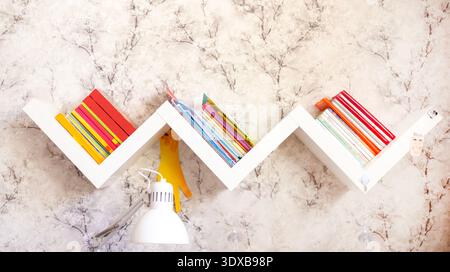 Zigzag bookshelf with books on a light wall Stock Photo