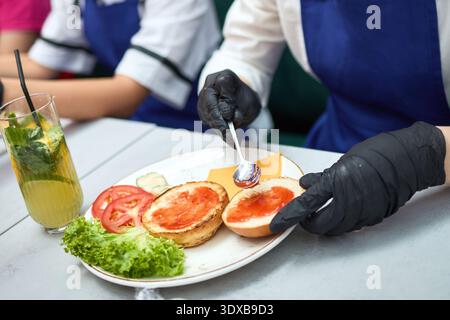 Chef spreads sauce on burger buns with spoon Stock Photo