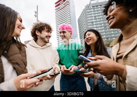 Diverse young friends having fun using mobile phones at city street Stock Photo