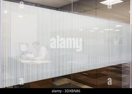 a man at a desk works behind a frosted glass office window Stock Photo