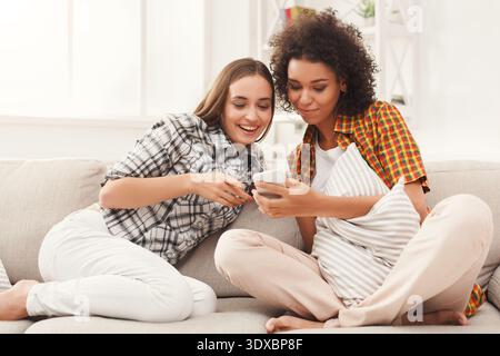 Two Friends Look at a Smartphone While Sitting on a Couch in a Bright Room During the Afternoon Stock Photo