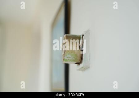 Close up side view of an old damaged wall electrical outlet with cracked plastic cover and visible corrosion showing unsafe wiring conditions indoors. Stock Photo