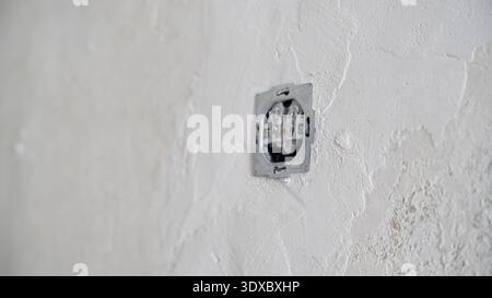 Unfinished electrical wall socket without cover installed in rough plastered wall during apartment renovation process. Stock Photo