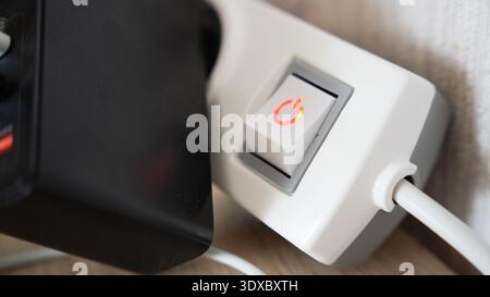 Close up of illuminated power switch with red light on white extension socket indoors. Stock Photo