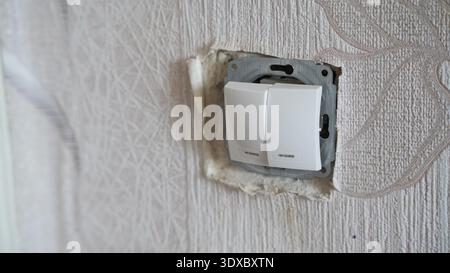 Double white wall light switch installed in textured wallpaper during interior renovation process. Stock Photo