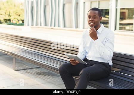 Man Sitting on a Bench Using a Tablet in an Outdoor Setting During a Sunny Day Stock Photo
