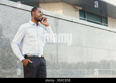 Man Stands by Building Making a Phone Call in a City During the Day Stock Photo
