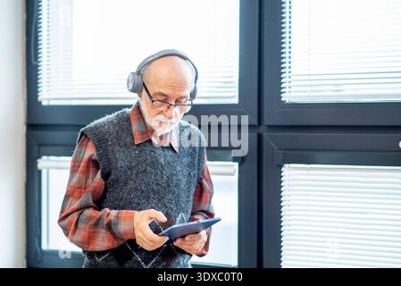 Senior man using tablet and headphones. Senior man using tablet and headphones at home. model released Stock Photo