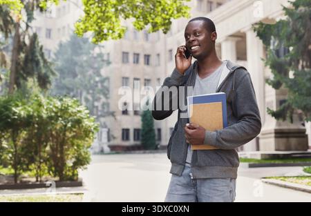 Student Talks on the Phone While Holding Notebooks in a University Courtyard During the Day Stock Photo