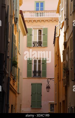Narrow alley in Monaco old town with pastel pink building, green shutters and wrought iron balcony under sunny skies.Monte Carlo, Monaco Stock Photo