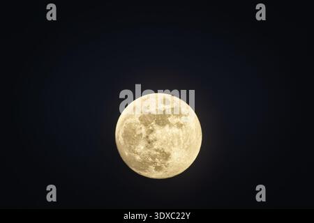 Close-up of a gibbous moon visible during the day, partially covered by soft wispy clouds in a blue sky. Stock Photo