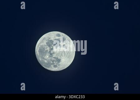 Close-up of a gibbous moon visible during the day, partially covered by soft wispy clouds in a blue sky. Stock Photo