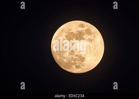 Close-up of a gibbous moon visible during the day, partially covered by soft wispy clouds in a blue sky. Stock Photo