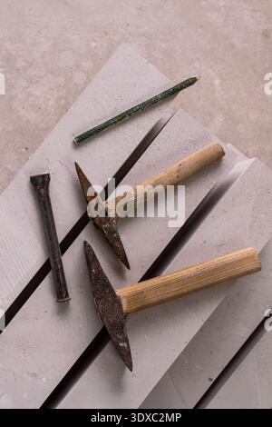 Marble mason tools displayed on a white marble slab in a stone workshop. The set includes two hammers with wooden handles and rusty metal heads, a gre Stock Photo