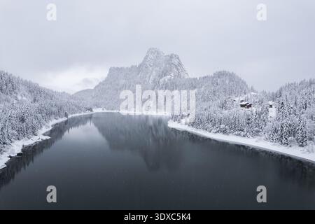 Aerial view of a tranquil lake mirroring snow-laden mountains and frosted forests under a muted sky, Vouvry, Valais, Switzerland. Stock Photo
