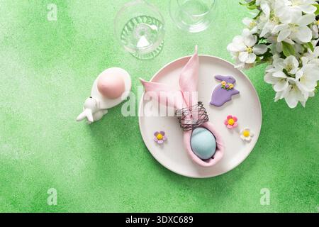 A beautifully arranged table setting for Easter features a pink napkin wrapped around an egg, surrounded by floral decorations and colorful candies. Stock Photo