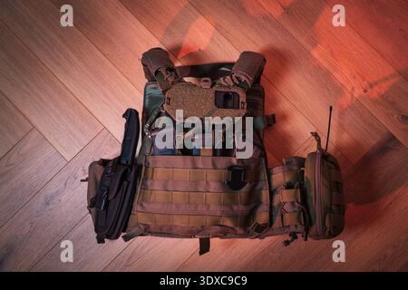 Full Tactical Plate Carrier with Magazines Knife and Radio Pouch on Wooden Floor Under Red Dramatic Lighting for Combat Mission. Stock Photo