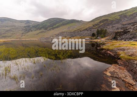 Abandoned spoil tips of the Cwmorthin slate mine are reflected in a lake in the mountains of Snowdonia. Stock Photo