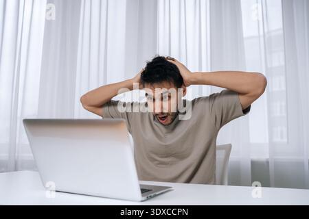 Portrait of shocked man reacting with shock and frustration, seeing bad online news or notification on laptop, feeling stressed and overwhelmed by Stock Photo