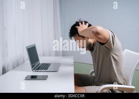 Stressed man finding shocking problem on laptop, reacting in frustration and stress with hands on head, representing issues, mistakes and burnout Stock Photo