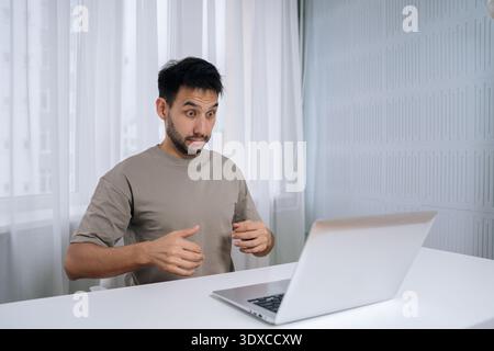 Shocker freelancer young man reacting with shock and confusion during remote work, experiencing technical problem or unexpected computer error while Stock Photo
