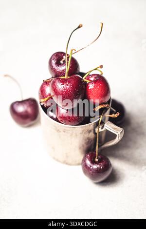 Small metal cup overflowing with fresh cherries. Low depth of field. Stock Photo
