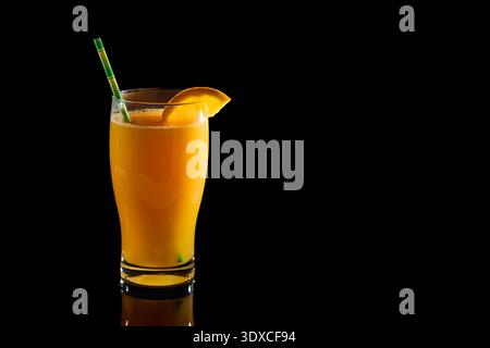 Orange juice in a glass, garnished with a citrus slice and a green straw, against a dark black background Stock Photo