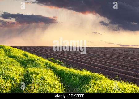 Plowed earth under dramatic sunset sky with approaching rain clouds. Rural agriculture, moody weather, farming landscape, seasonal work Stock Photo