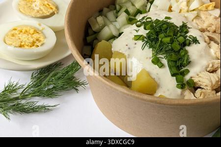 Chopped ingredients for okroshka in a bowl on the table. Russian traditional cold soup with half a boiled egg, greens, onion Stock Photo