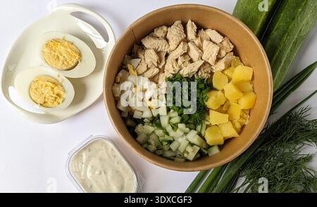 Chopped ingredients for okroshka in a bowl on the table. Russian traditional cold soup with half a boiled egg, greens, onion Stock Photo