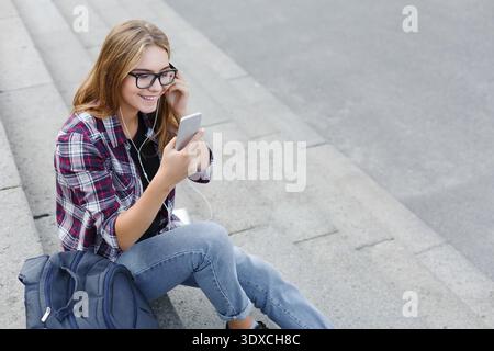 Girl Sitting on Steps Enjoying Music While Using Smartphone Stock Photo