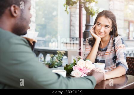 Couple Enjoys Conversation Over Coffee at Outdoor Cafe While Flowers Sit on the Table Stock Photo