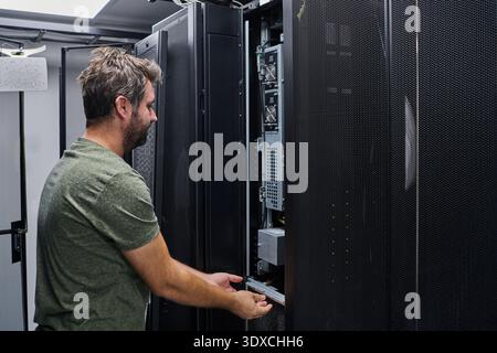 IT technician performing server maintenance in a data center rack during routine equipment inspection Stock Photo