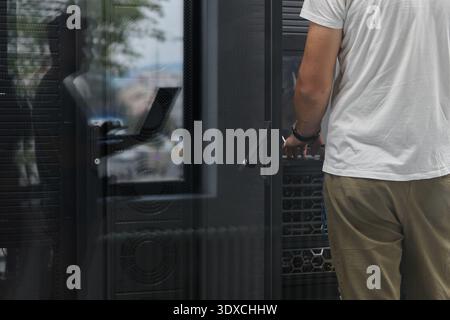 IT technician working on server rack in office data center with visible network equipment and reflection Stock Photo