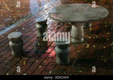 Wet Stone Table and Stools on Brick Pavement with Fallen Leaves in Shanghai, China Stock Photo
