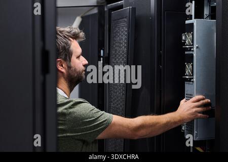 It technician servicing a server rack in a data center performing hardware maintenance and inspection Stock Photo