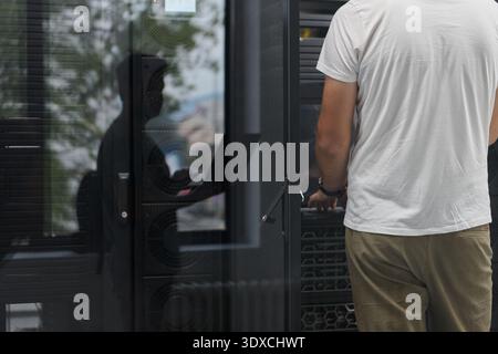 IT technician working on a server rack in a data center, rear view of man maintaining hardware Stock Photo