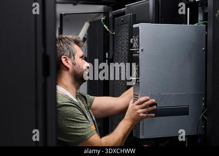 IT technician installing server hardware in a data center rack performing maintenance and network setup Stock Photo