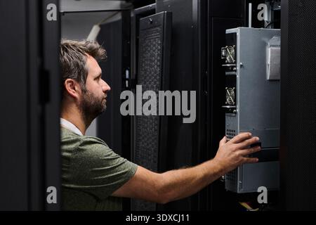 It technician installing and inspecting server hardware in a data center server rack during maintenance Stock Photo
