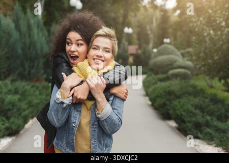Two Friends Enjoy a Fun Moment While Hugging Each Other in a Park Setting During Daylight Hours Stock Photo