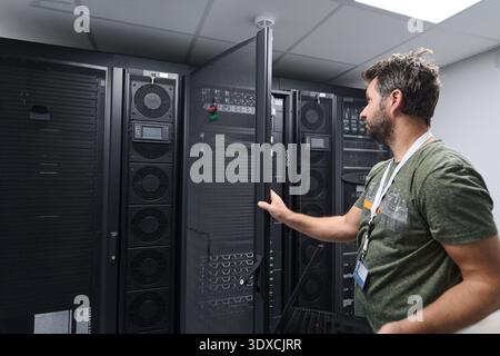 IT technician inspecting server racks in a data center with network equipment and monitoring console Stock Photo