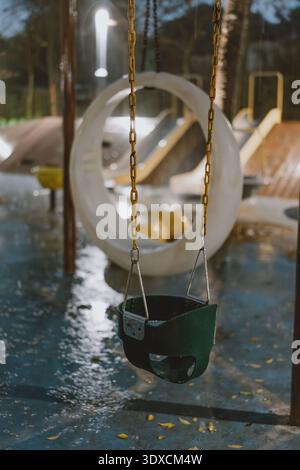 Empty green baby swing hanging on chains at wet playground in Shanghai, China, with circular tire Stock Photo